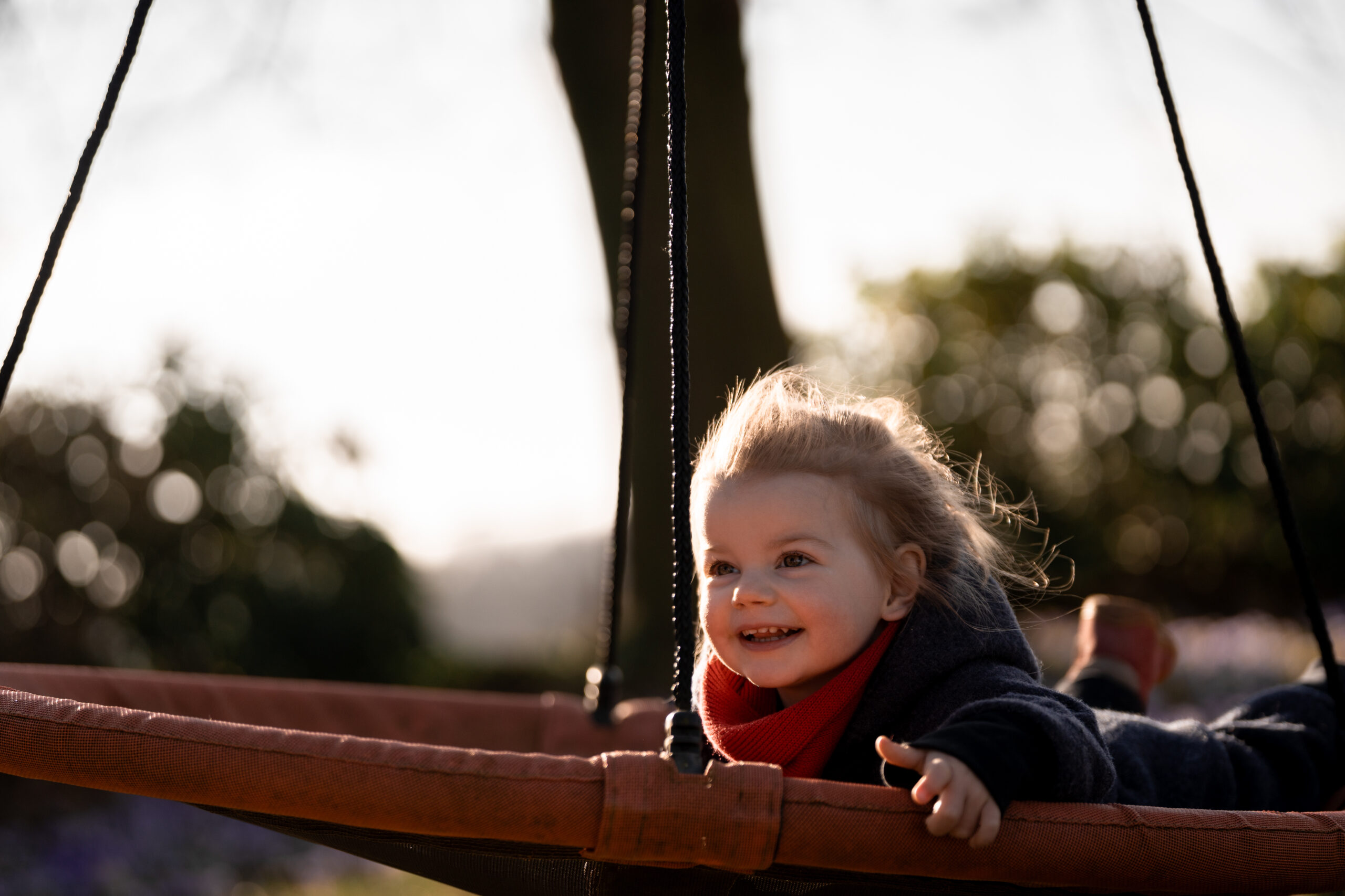 Kleinkind mit leicht wehenden Haaren liegend auf einer großen Schaukel in Melle